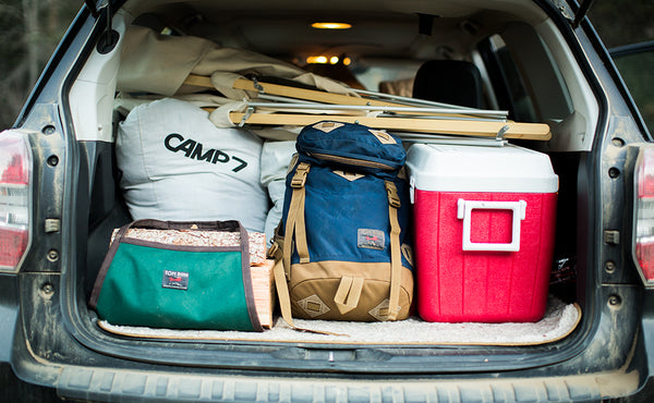 A Firewood Carrier with wood packed into the hatch of a car filled with camping gear.